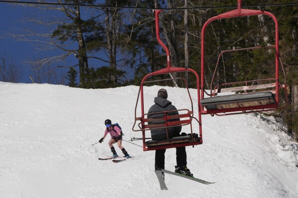 A skier wearing shorts heads down a trail as a rider takes a chair lift to the summit at Black Mountain, Friday, March 14, 2025, in Jackson, N.H. (AP Photo/Charles Krupa)
