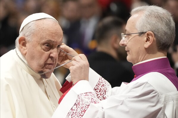 Pope Francis is helped by his aide Archbishop Diego Giovanni Ravelli, right, as he arrives for the start of a public consistory to elevate 21 new cardinals, in St. Peter's Basilica, at the Vatican, Saturday, Dec. 7, 2024. (AP Photo/Gregorio Borgia, file)