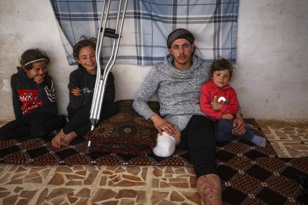 Suleiman Khalil, 21, who lost his leg in a landmine explosion while harvesting olives with his friends in a field, poses for a pictures with his siblings from left to right, Sakina, 8, Nahla, 9, and Aya, 5, at his home in the village of Qaminas, east of Idlib, Syria, Wednesday, April 9, 2025. (AP Photo/Ghaith Alsayed)