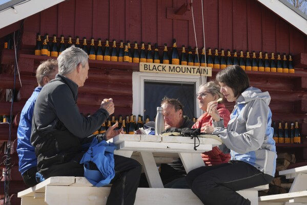 Skiers enjoy their lunch on picnic tables outside the Alpine Cabin, a mid-slope refreshment stop, at Black Mountain, Friday, March 14, 2025, in Jackson, N.H. (AP Photo/Charles Krupa)